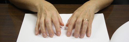 A pair of hands "reading" a sheet containing braille.