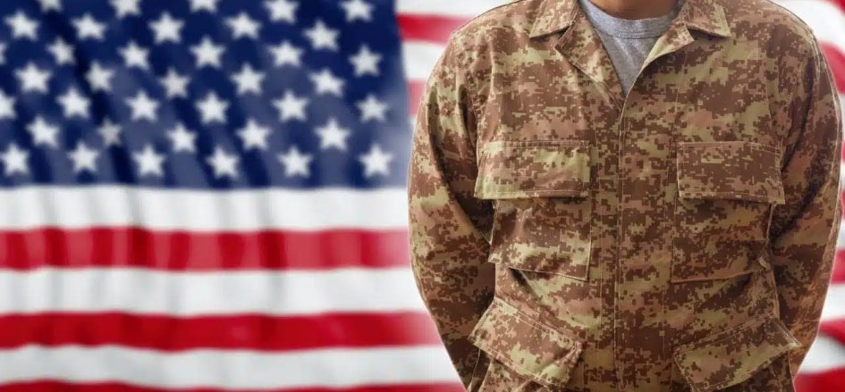 Image of a soldier standing in front of an American flag