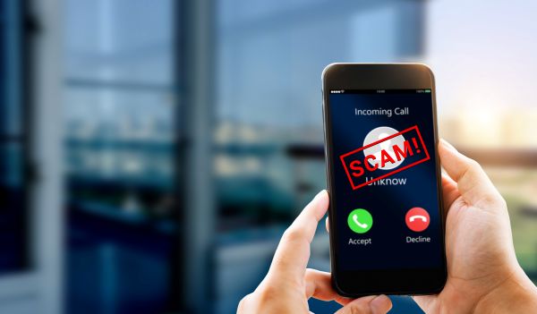 A person touches a laptop surrounded by floating icons: a red warning sign labeled SCAM, a hooded figure, an ID card, a credit card, a microphone, an email alert and an Unknown Calling phone icon.